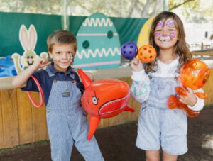 Two children are at Irvine Park Railroad's carnival game while they hold inflatable toys, rings, and balls that are used to participate in the activity