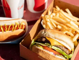 Two children are at Irvine Park Railroad's carnival game while they hold inflatable toys, rings, and balls that are used to participate in the activity A serving tray with a fresh hamburger, fries, hot dogs, and Coca Cola drinks from Irvine Park Concessions