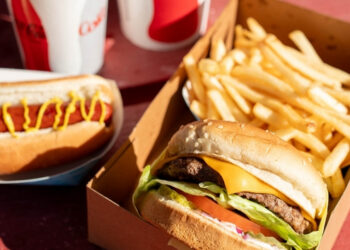 A serving tray with a fresh hamburger, fries, hot dogs, and Coca Cola drinks from Irvine Park Concessions