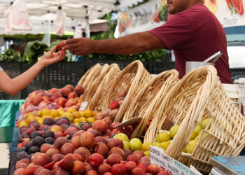 A farmer's stand at the farmer's market at Irvine Regional Park hands a customer a sample