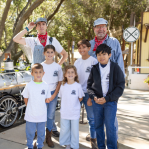 Children and adults smile at Irvine Park Railroad's Junior Engineer Program in front of the locomotive