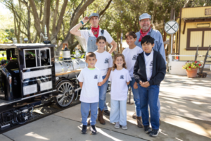 Children and adults smile at Irvine Park Railroad's Junior Engineer Program in front of the locomotive